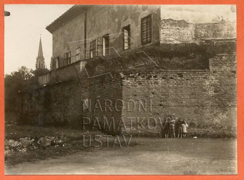 Historická fotografie dochovaného fragmentu hradební zdi s budovou pekárny v pozadí